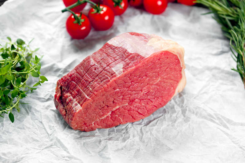 在白色背景下的一块新鲜的肉用绿色和蔬菜装饰