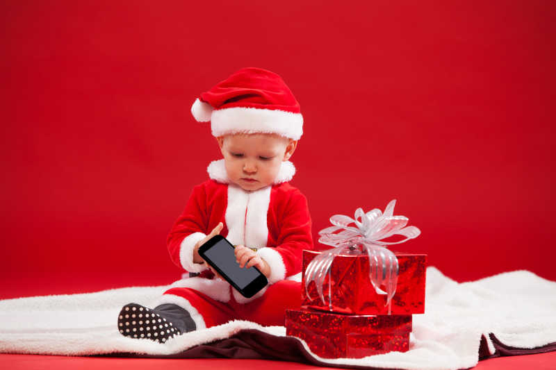 美丽的小婴儿带着礼物和电话庆祝圣诞节