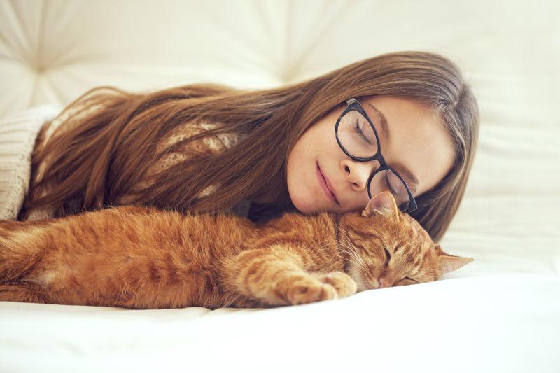 可爱的猫咪睡在戴眼镜的小女孩身边