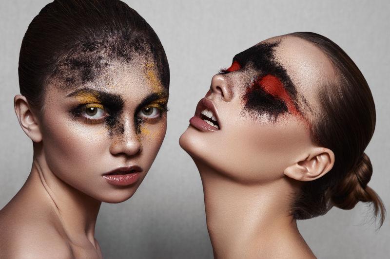 灰色背景下涂着浓重的黑红粉和黑黄粉的两个女模特