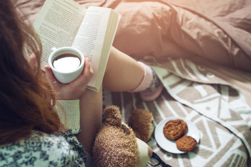 拿着咖啡在床上看书的女孩