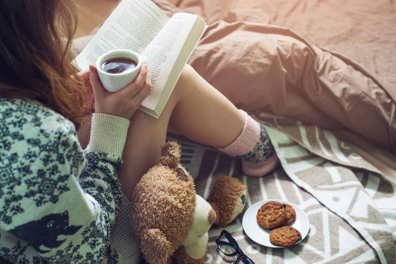 手拿咖啡坐在床上看书的女孩