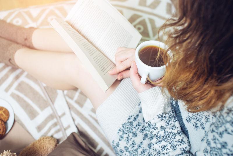 女孩坐在床上端着咖啡看书