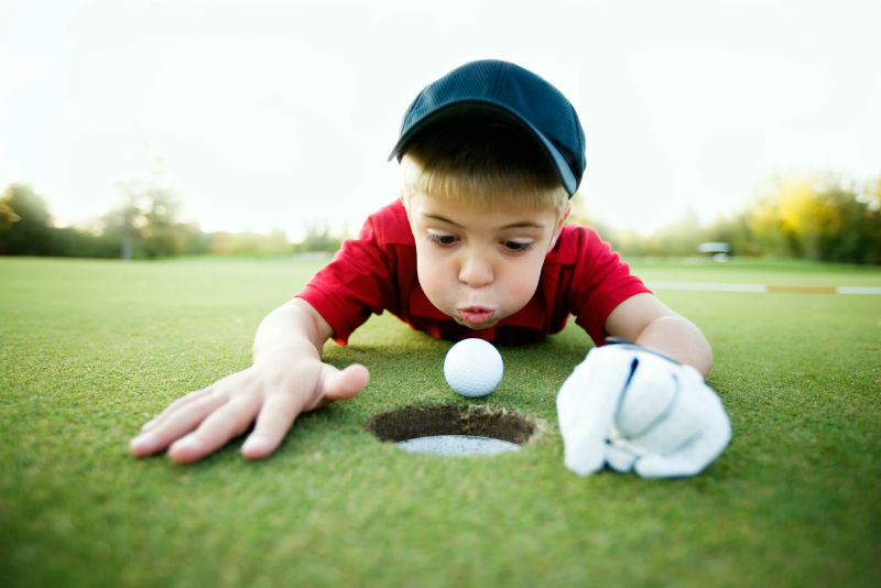 男孩把高尔夫球吹到高尔夫球洞里