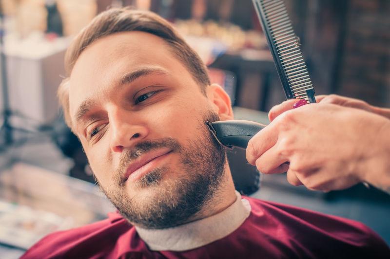 理发师在理发店用修剪器为男子刮胡子