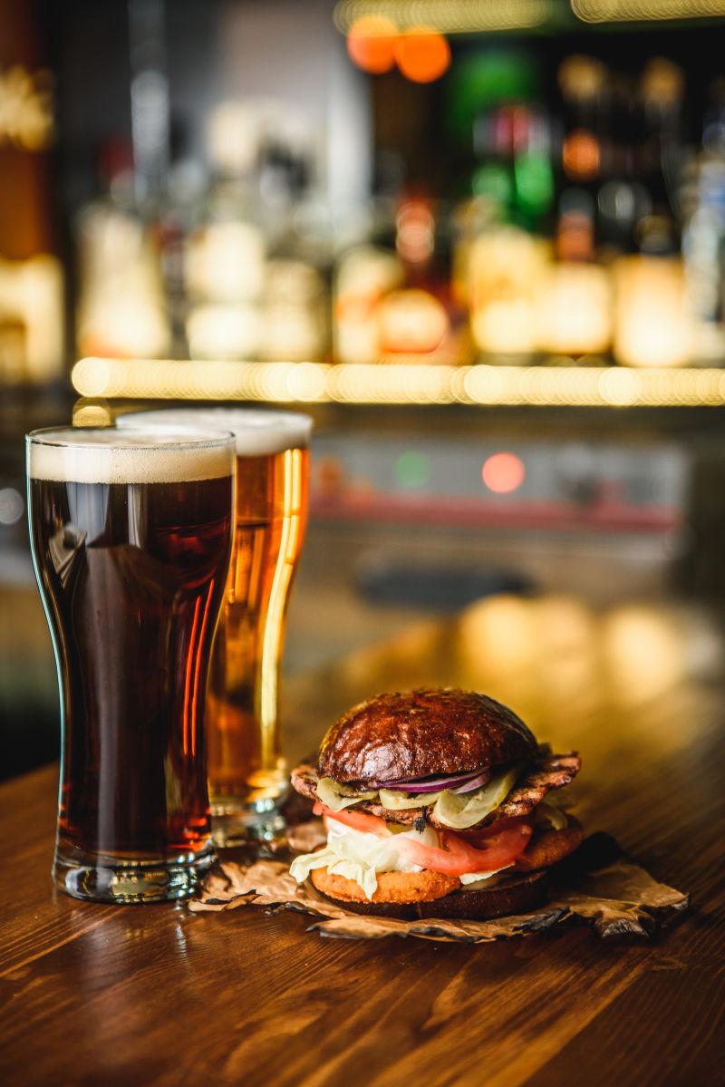酒吧背景下木制吧台上的汉堡包和黑啤酒