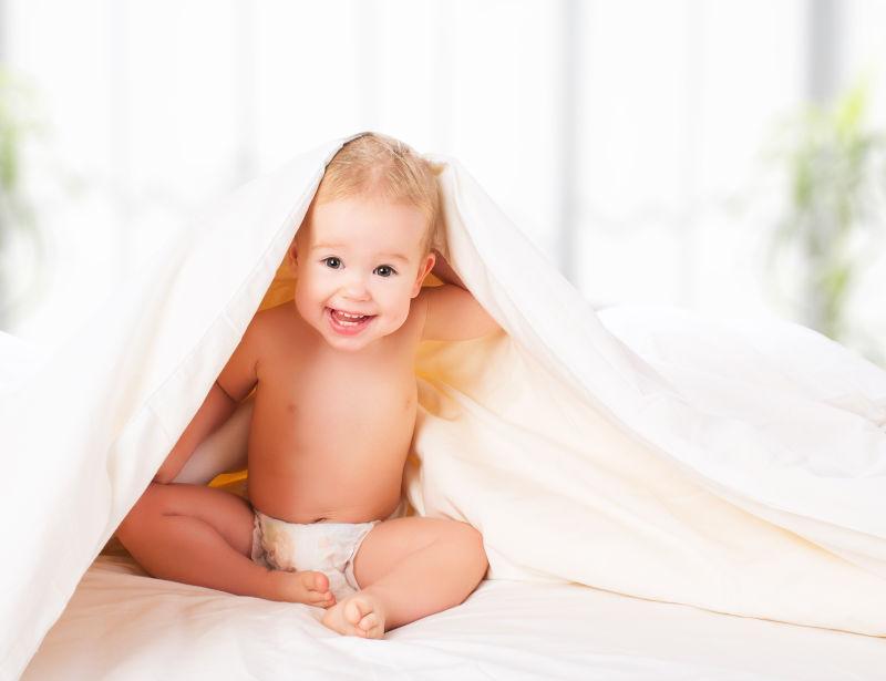 在毯子下欢笑的快乐的婴儿