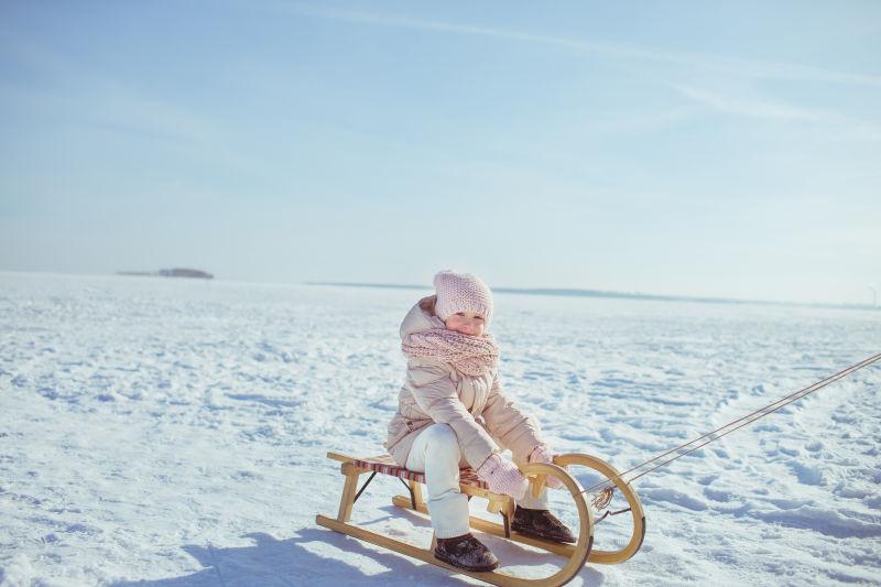 小女孩坐在雪橇上玩雪