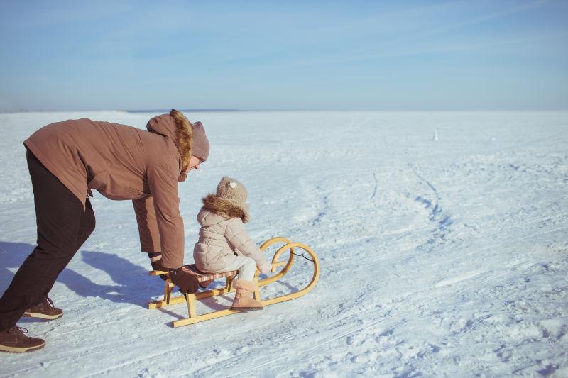 雪地里父亲用雪橇推他的女儿玩耍