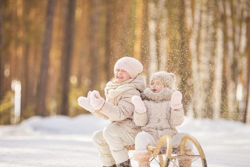 坐在雪橇上玩雪的两个小女孩