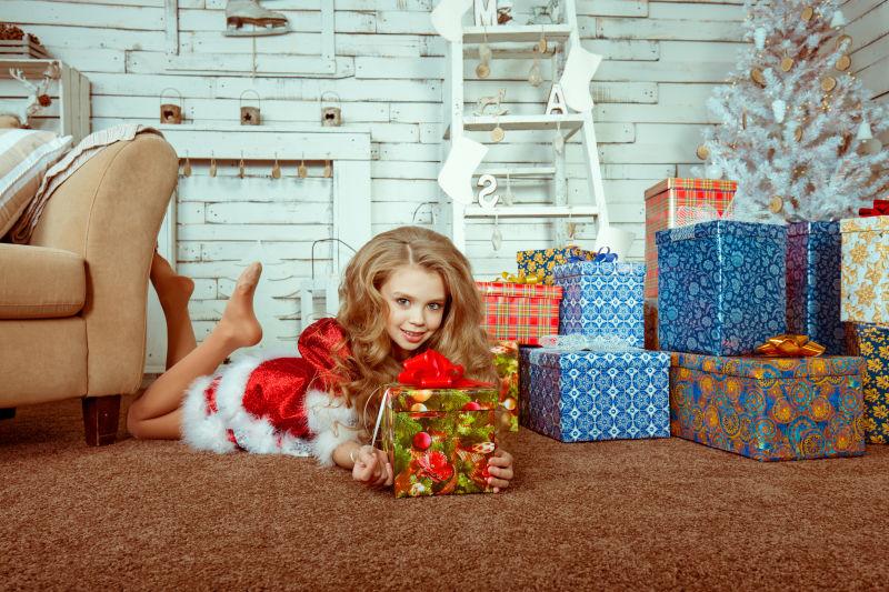 手拿圣诞礼物的小女孩趴在地板上