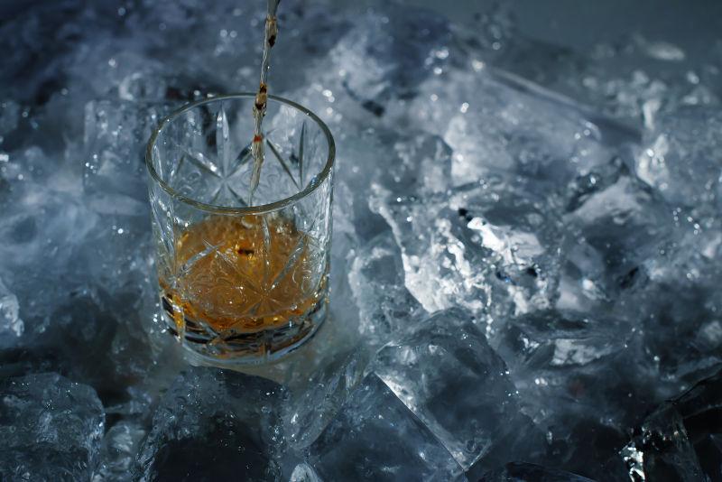 在明亮的灯光下拍摄大块的冰块和威士忌玻璃杯