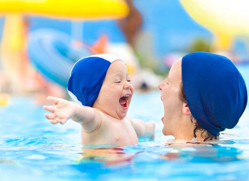 快乐的孩子和带泳帽的妈妈在泳池里玩得开心