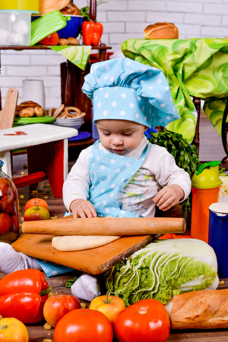 穿着厨师衣服的婴幼儿在厨房里擀面