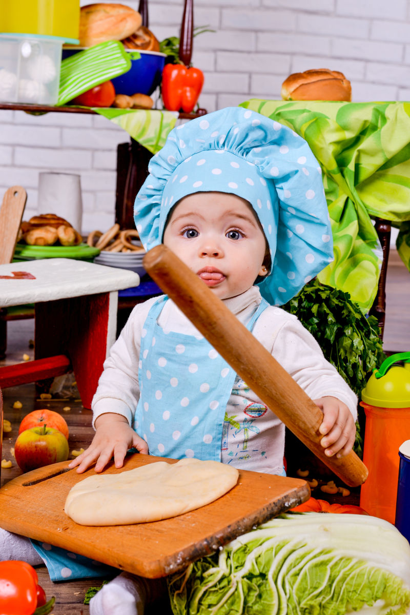 穿着厨师衣服的小宝贝在厨房里擀面