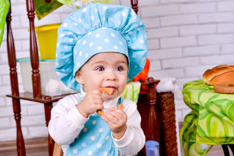 穿着厨师衣服的幼儿在吃百吉饼