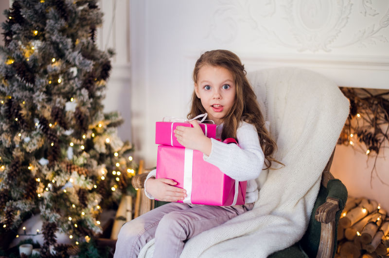 圣诞树旁边凳子上小女孩