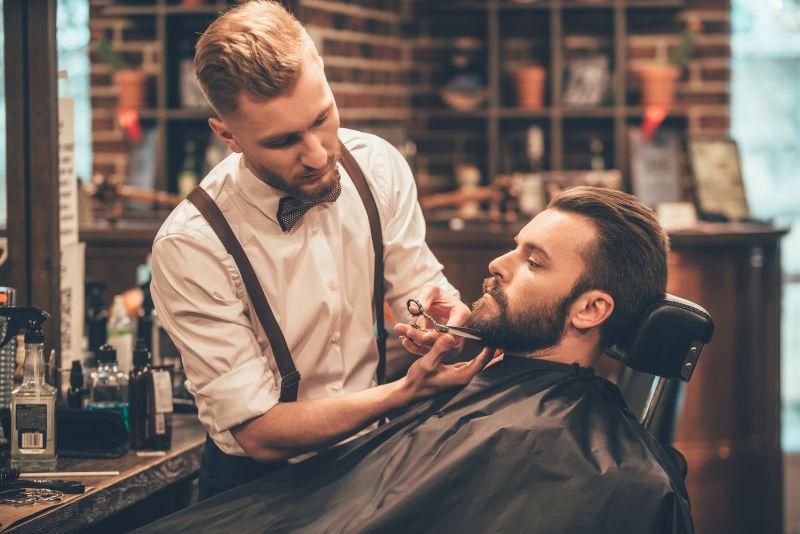 理发师给年轻的胡子男人剪胡子