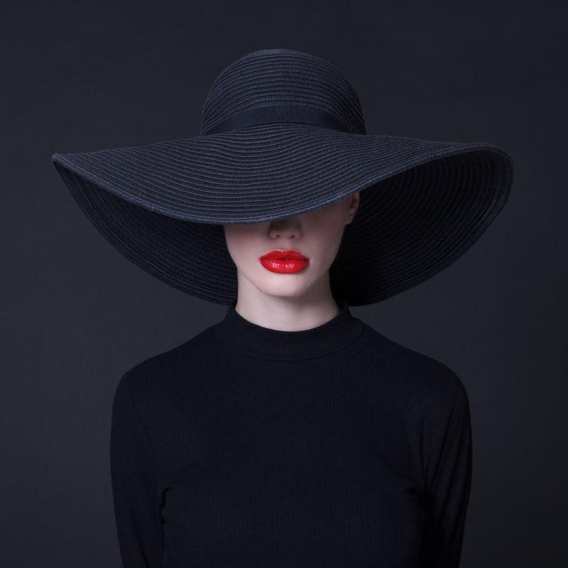 在黑色背景下红嘴唇戴着黑色大帽子的豪华女人