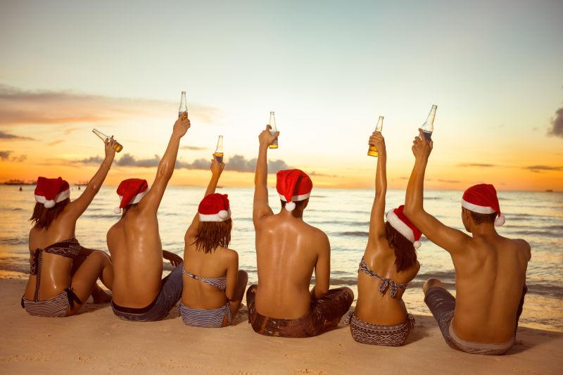坐在沙滩上一群戴着圣诞帽子的年轻人