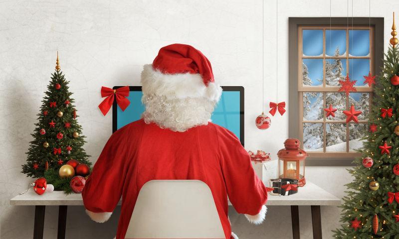 圣诞老人使用电脑和圣诞树和装饰物