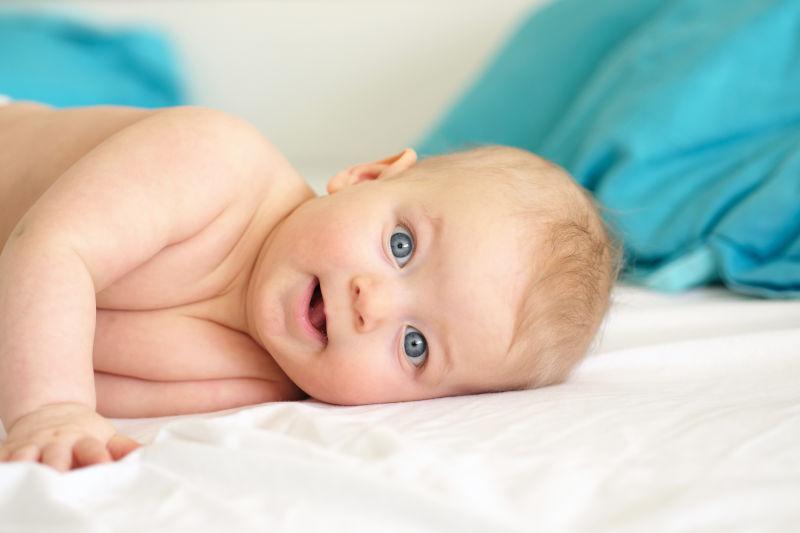 蓝眼睛的婴儿躺在白色毯子上的可爱表情