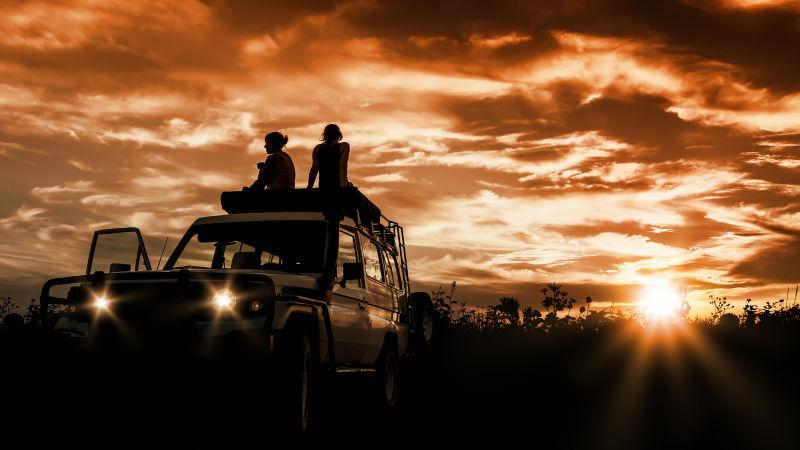 两个美女坐在越野车顶上看日落