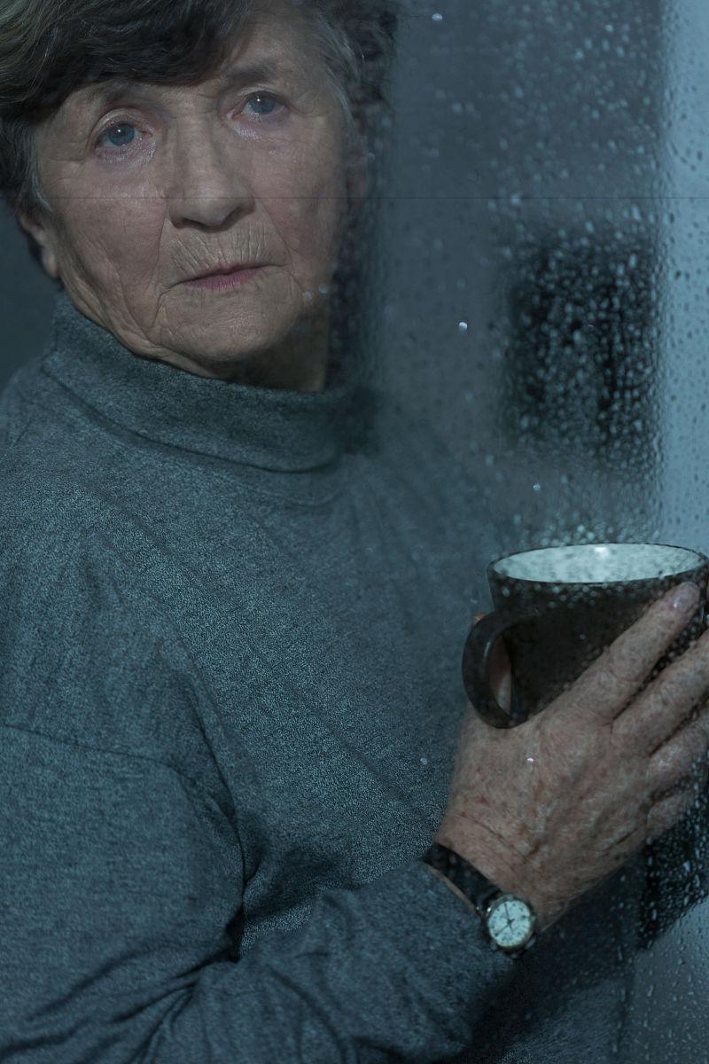 在下雨天站在窗边的老年人