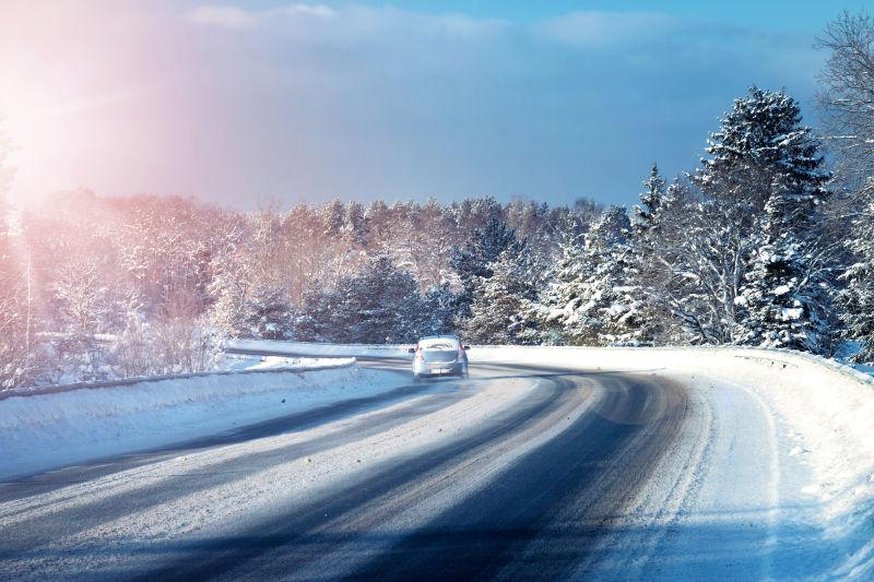 阳光下冬天覆盖着雪的路上的汽车
