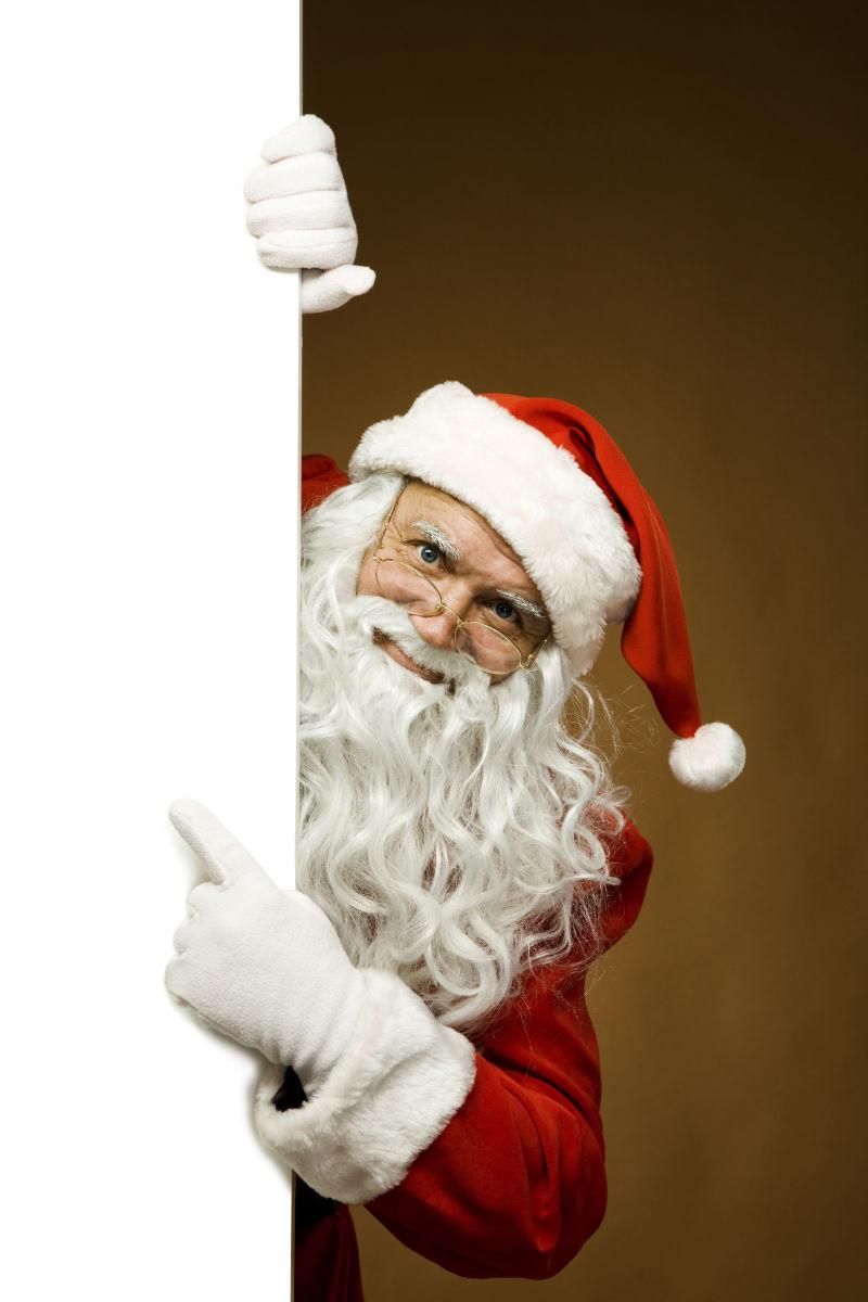 在白色广告牌后面的圣诞老人用手指着它
