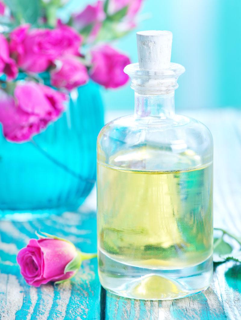 蓝色旧木桌上的玫瑰花和玻璃瓶里的精油