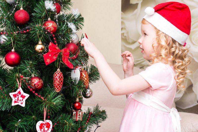 戴着圣诞帽子穿粉色裙子的小女孩在圣诞树下