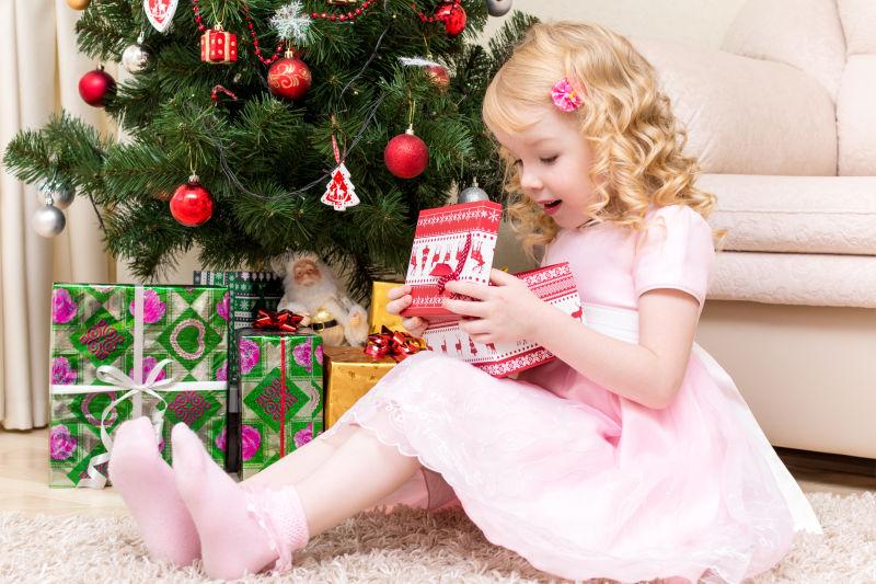 金发小女孩在圣诞树下打开礼物