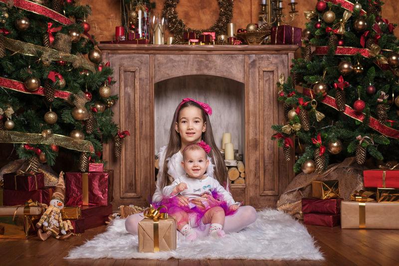 可爱的圣诞姐妹坐在圣诞树下白色地毯上