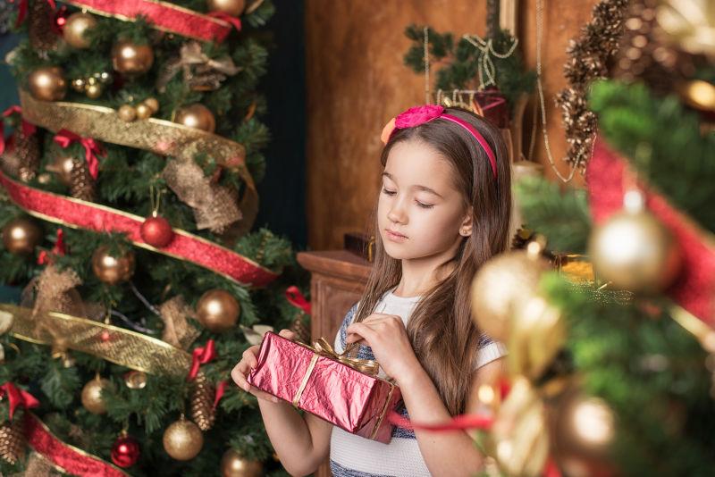 梦中的小女孩戴着红色头巾在圣诞树旁打开礼物