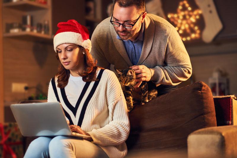 男人教戴着圣诞帽的美女如何使用笔记本电脑
