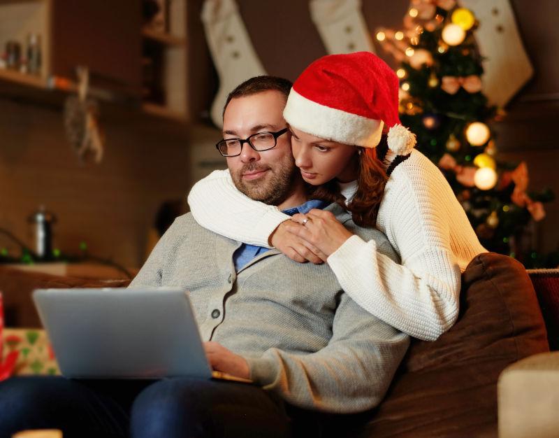戴着圣诞帽的美女搂着男子一起看着笔记本电脑