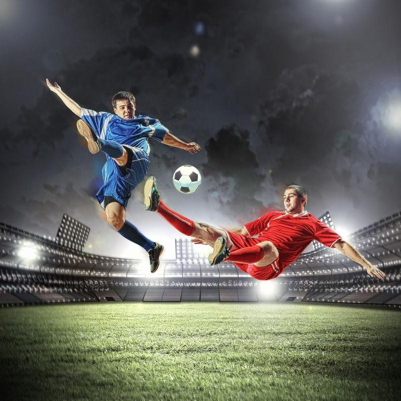 夜晚的足球场上两个穿着红色和蓝色运动服的足球运动员在踢足球