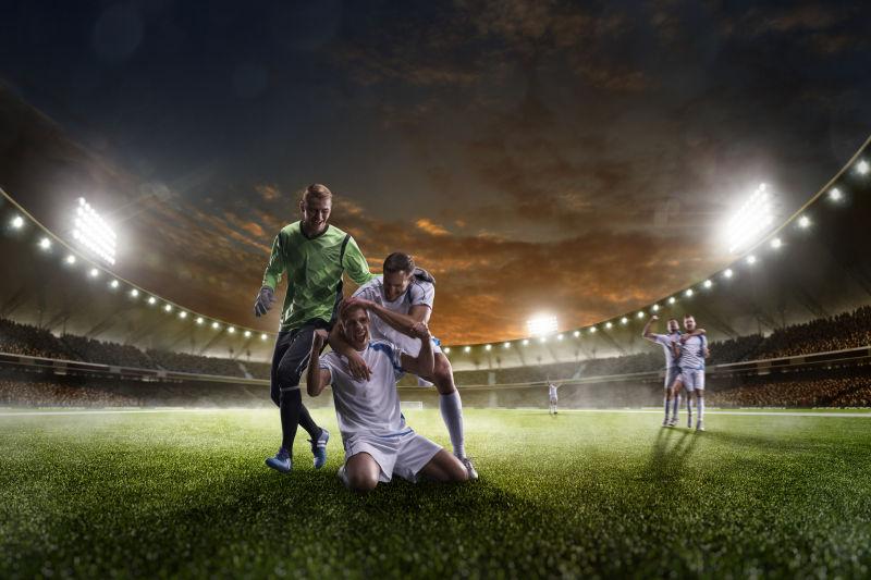 夜幕时分灯火通明的足球场上的开心的足球运动员