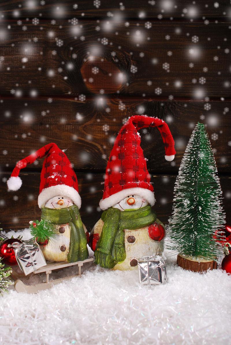 小圣诞树边两个带着红色圣诞帽的可爱雪人