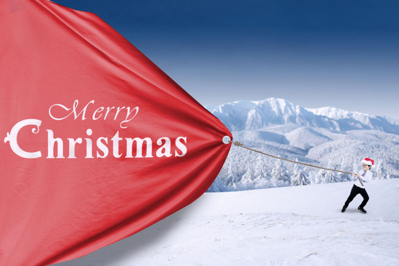 雪山上带着红色圣诞帽的男孩拉着一块红布