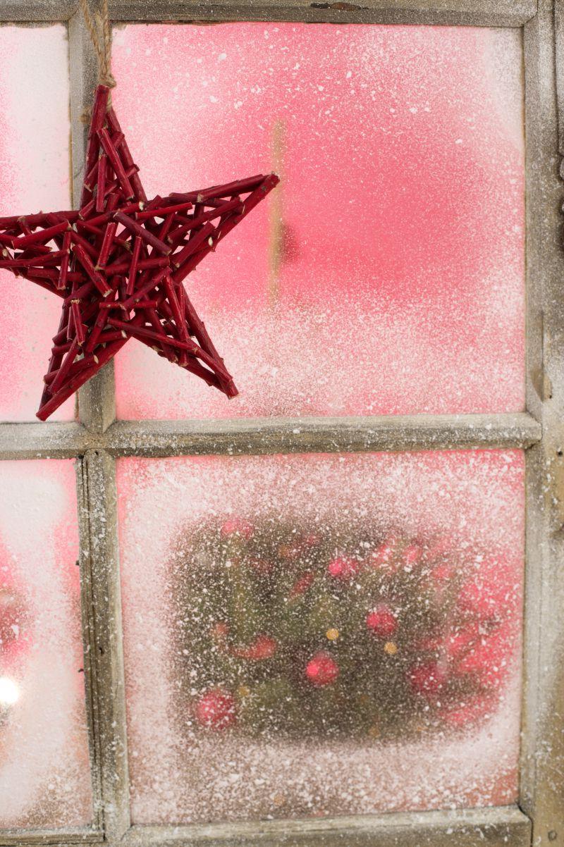 红色的圣诞五角星挂在满是雪霜的玻璃上