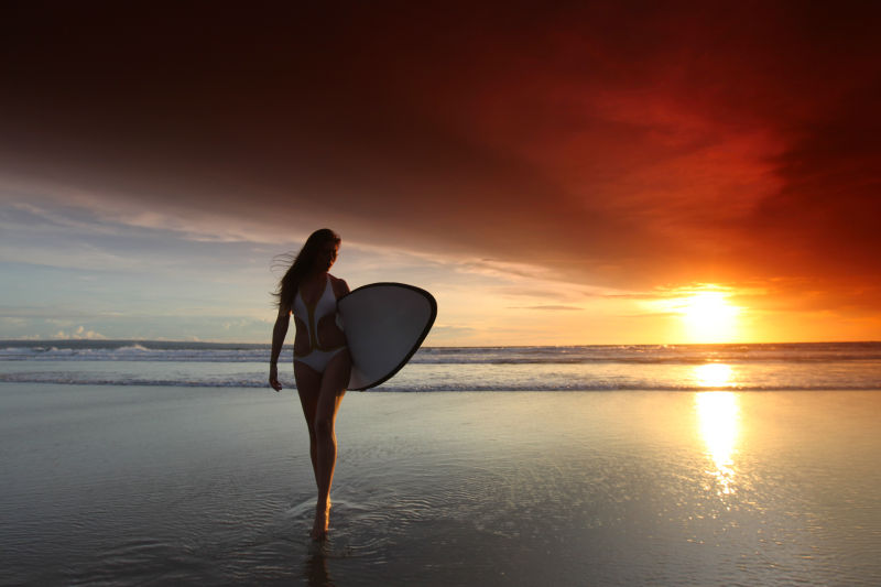 日落时美丽的冲浪女孩在沙滩上