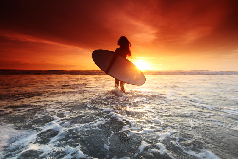 美丽的日落时海滩上冲浪女子
