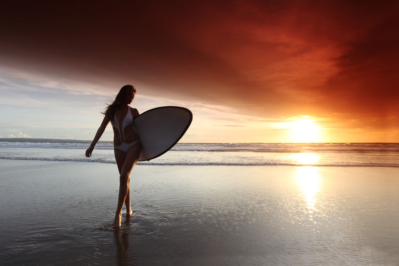 迷人的日落时分海滩上的冲浪女人