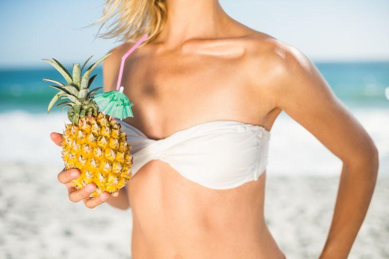 海滩上穿着白色胸衣的美女拿着一个菠萝
