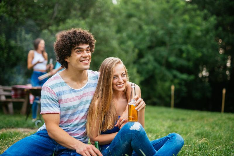年轻的情侣坐在草地上喝啤酒