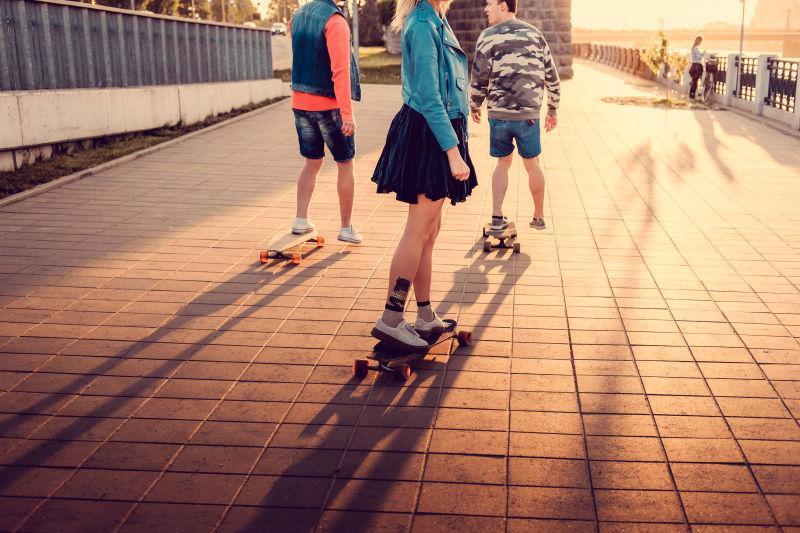 夕阳下城市道路上滑滑板车的三个年轻人