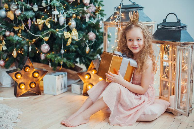坐在圣诞树旁抱着礼物的小女孩