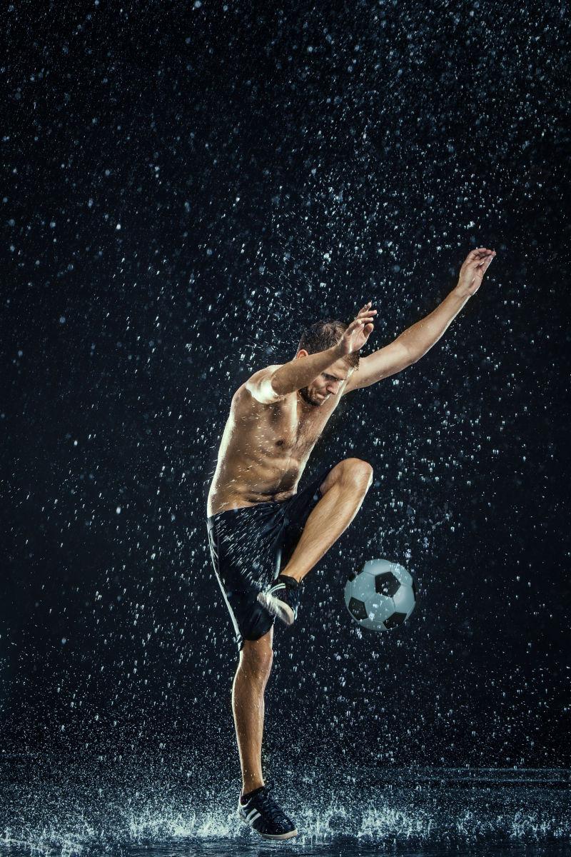 正在踢足球的运动员和水滴在黑色背景下